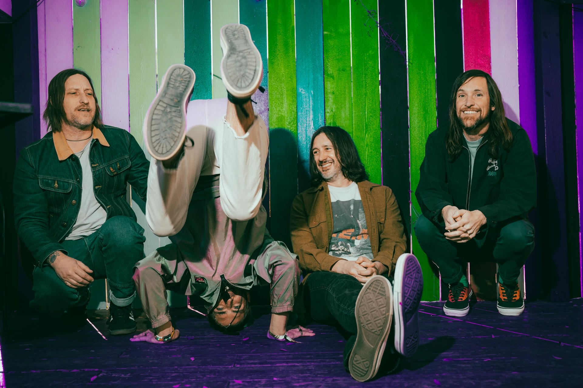 Four people sitting on a colorful striped floor with one person upside down.