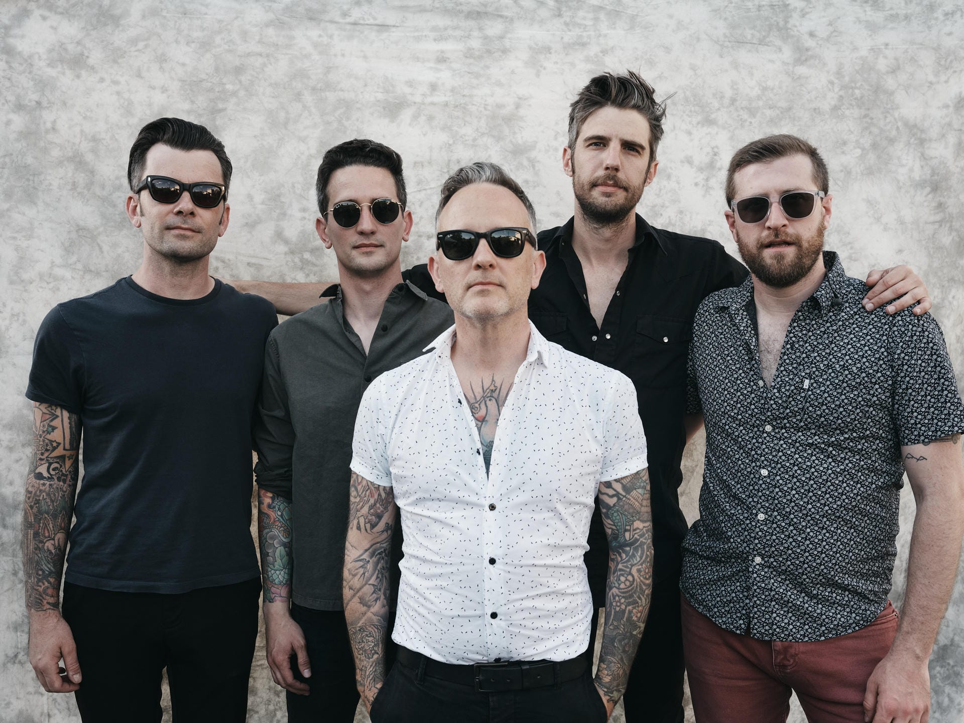 Five men posing together with sunglasses on a textured wall background