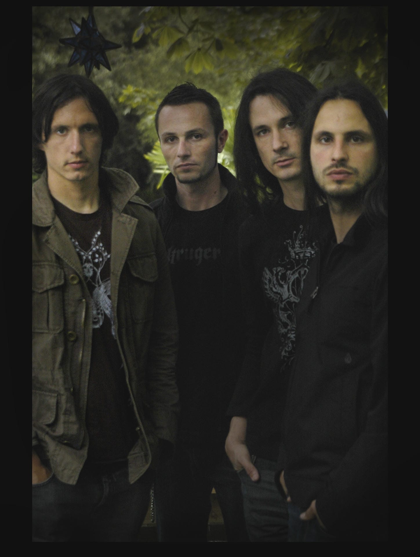Four individuals standing together with a dark, forest-like background