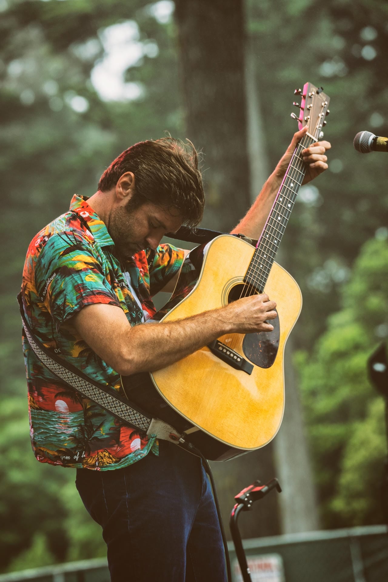 Man playing an acoustic guitar with a microphone in a natural setting