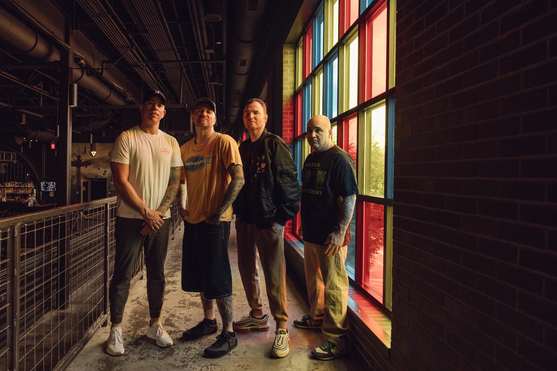 Four men standing in front of a colorful stained glass window in an urban setting.
