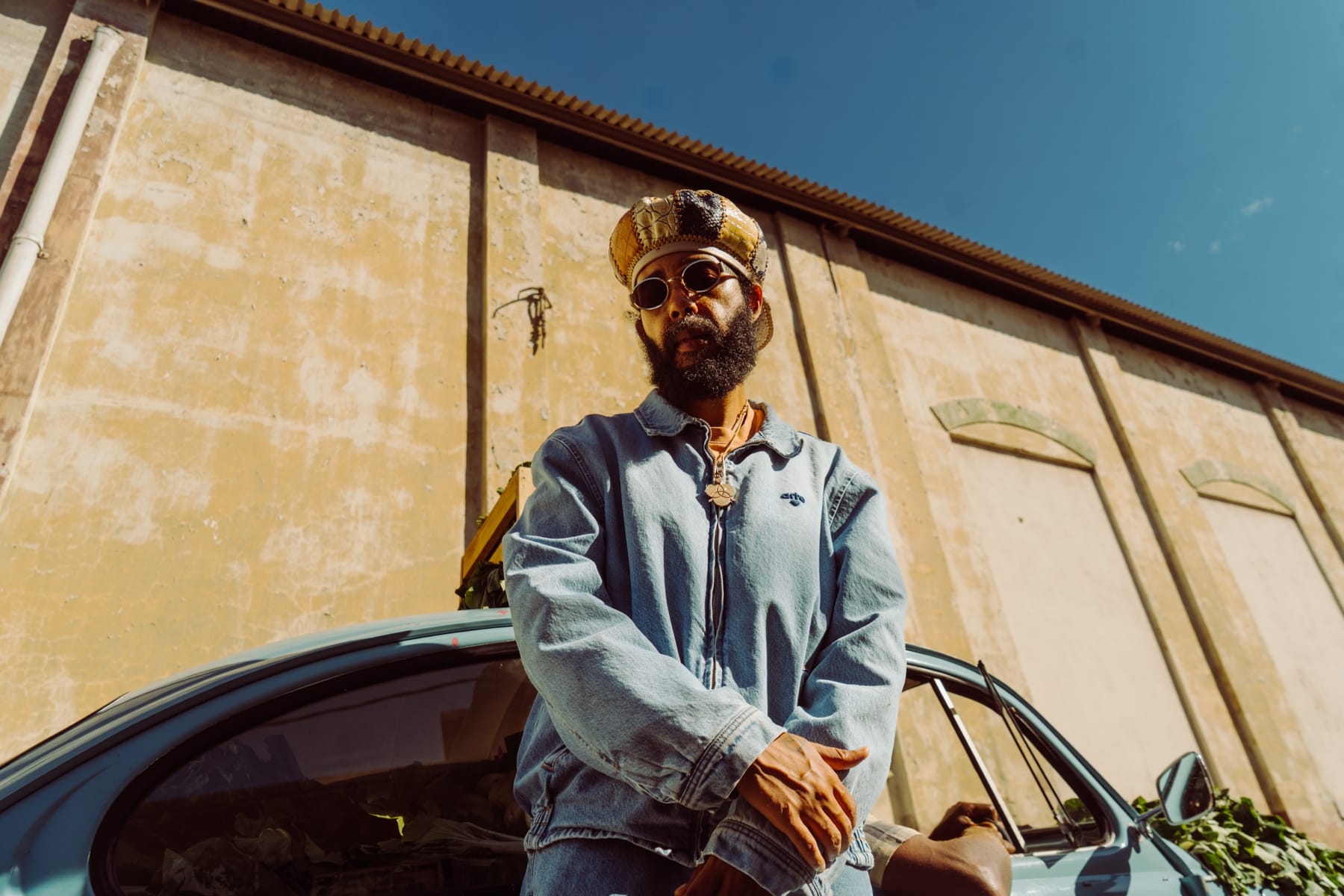 Man standing next to a car with a beige building and blue sky in the background