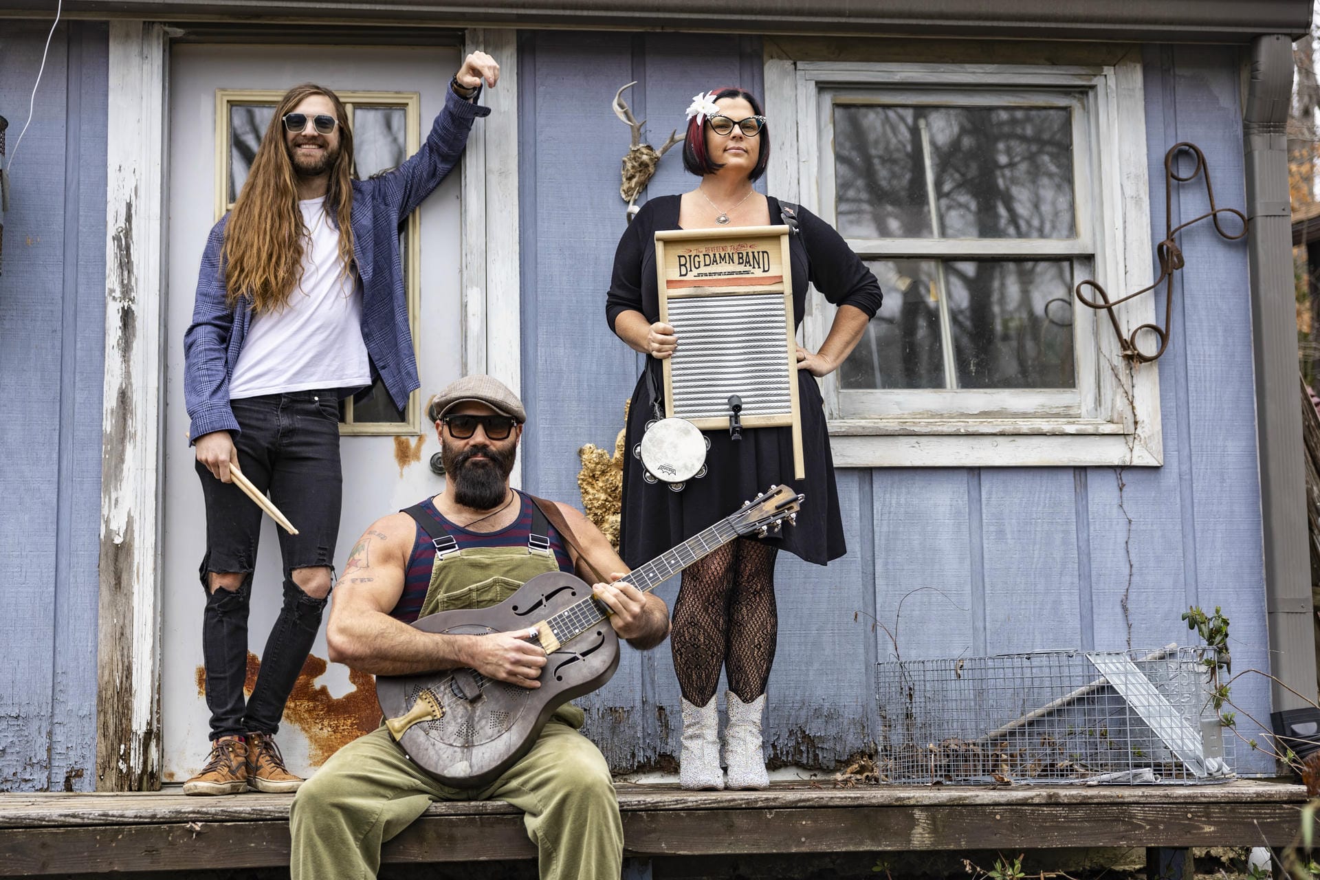 Three people posing in front of a blue building with musical instruments
