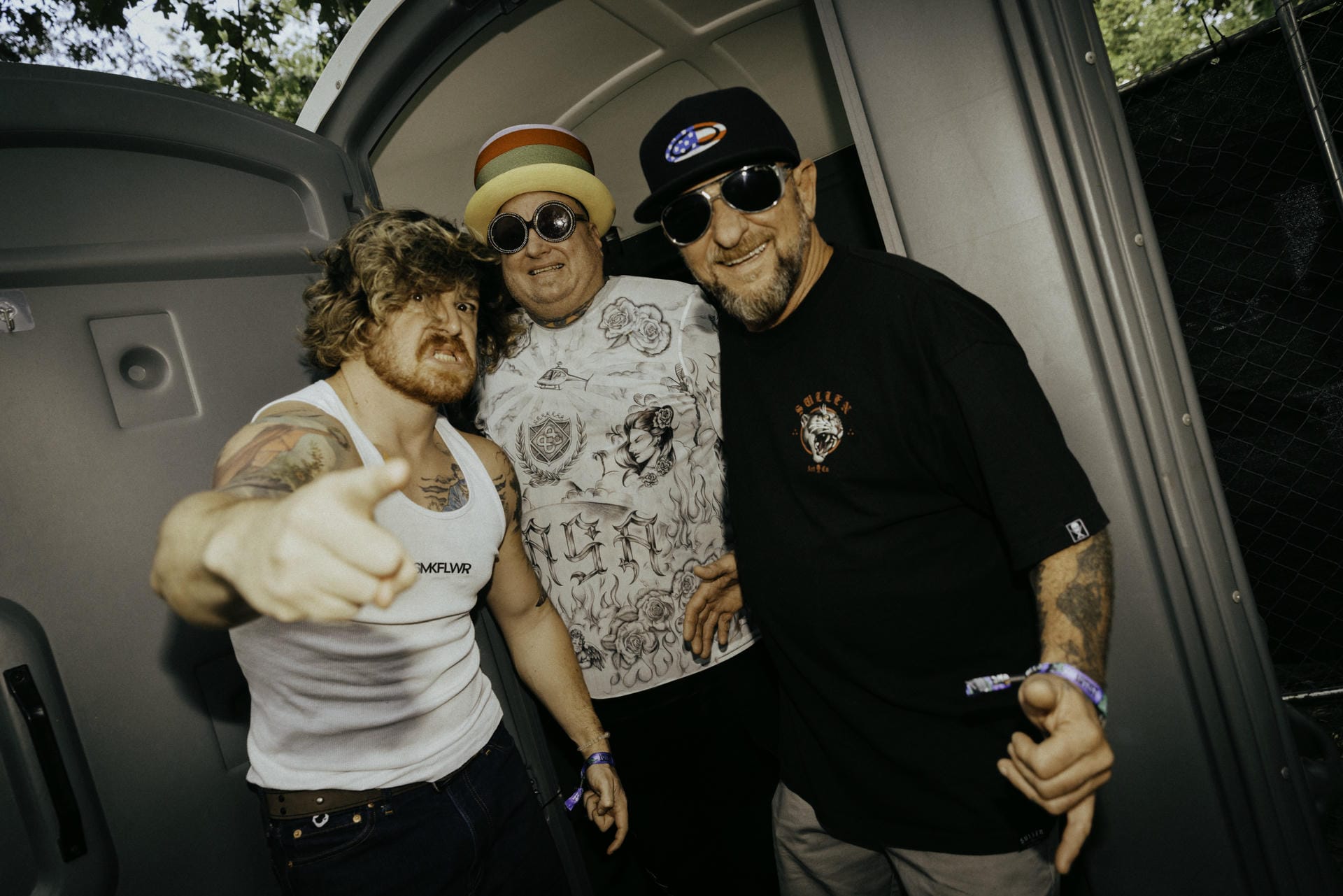 Three people posing together in a vehicle, with one pointing towards the camera.