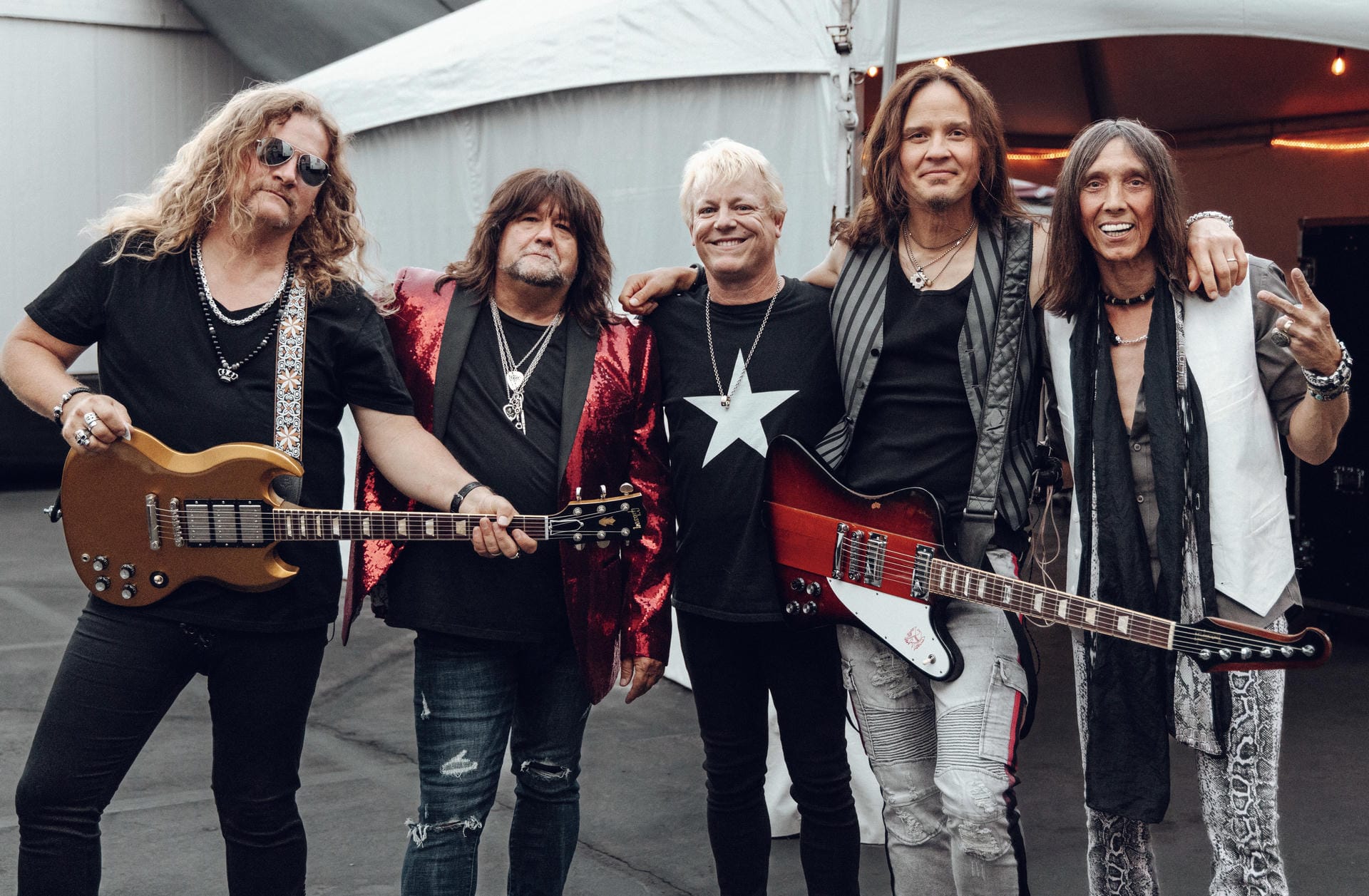 Five musicians posing together with guitars in an outdoor setting