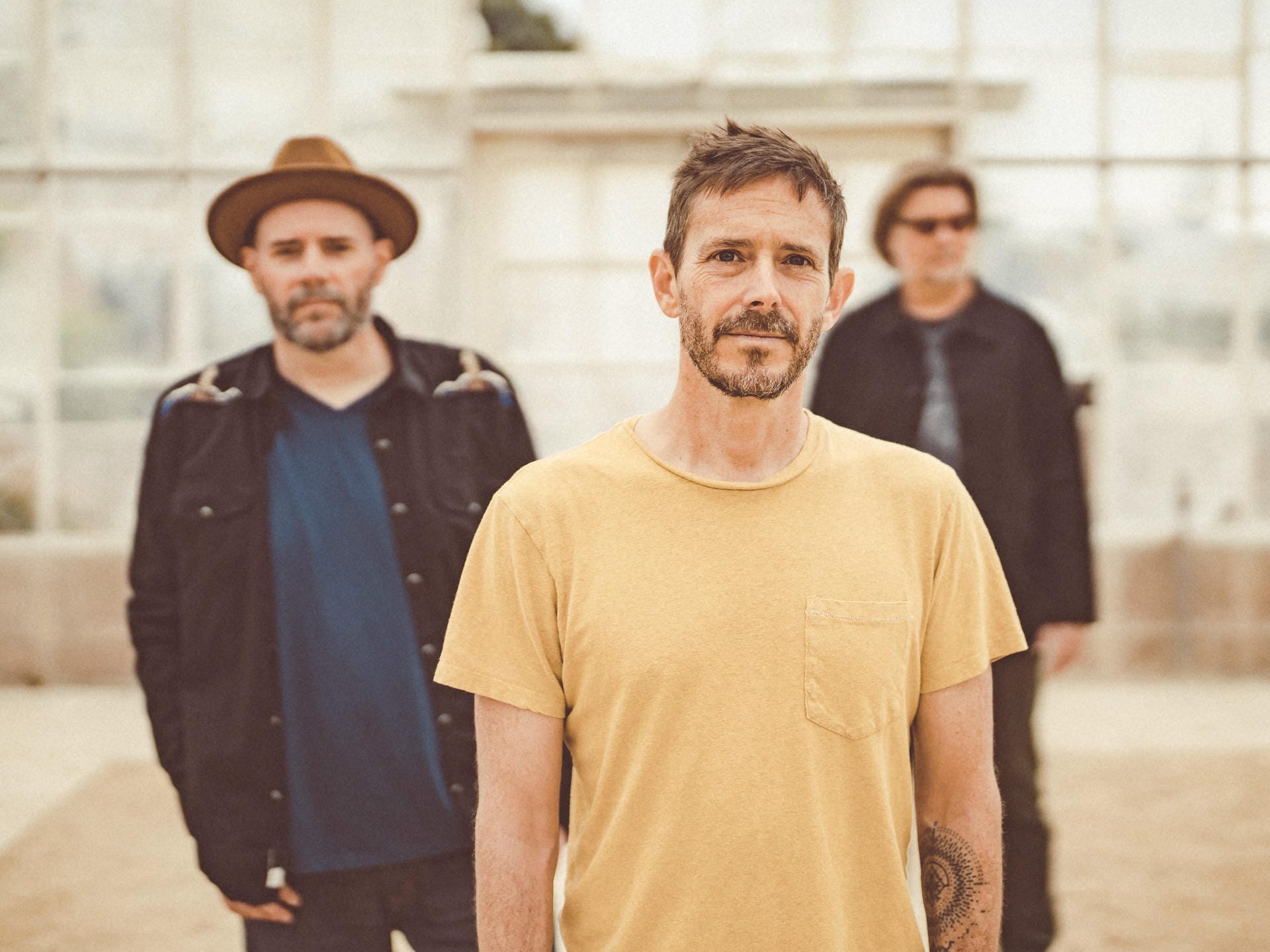 Three men standing outdoors with a neutral background